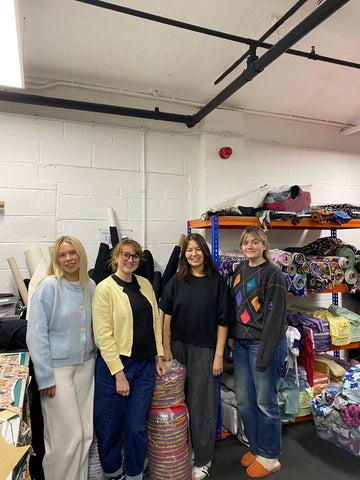 Picture shows 4 women smiling to the camera in a sewing studio with colourful Wilde Mode fabrics in the background