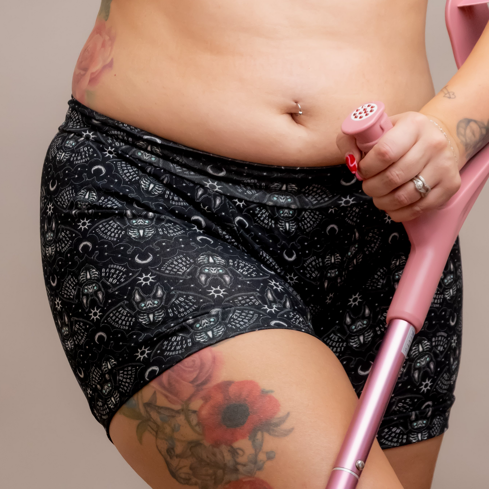 A close-up of a woman wearing a matching black and white celestial pattern activewear set, consisting of a sports bra and high-waisted shorts, holding a pink crutch against a solid beige background.