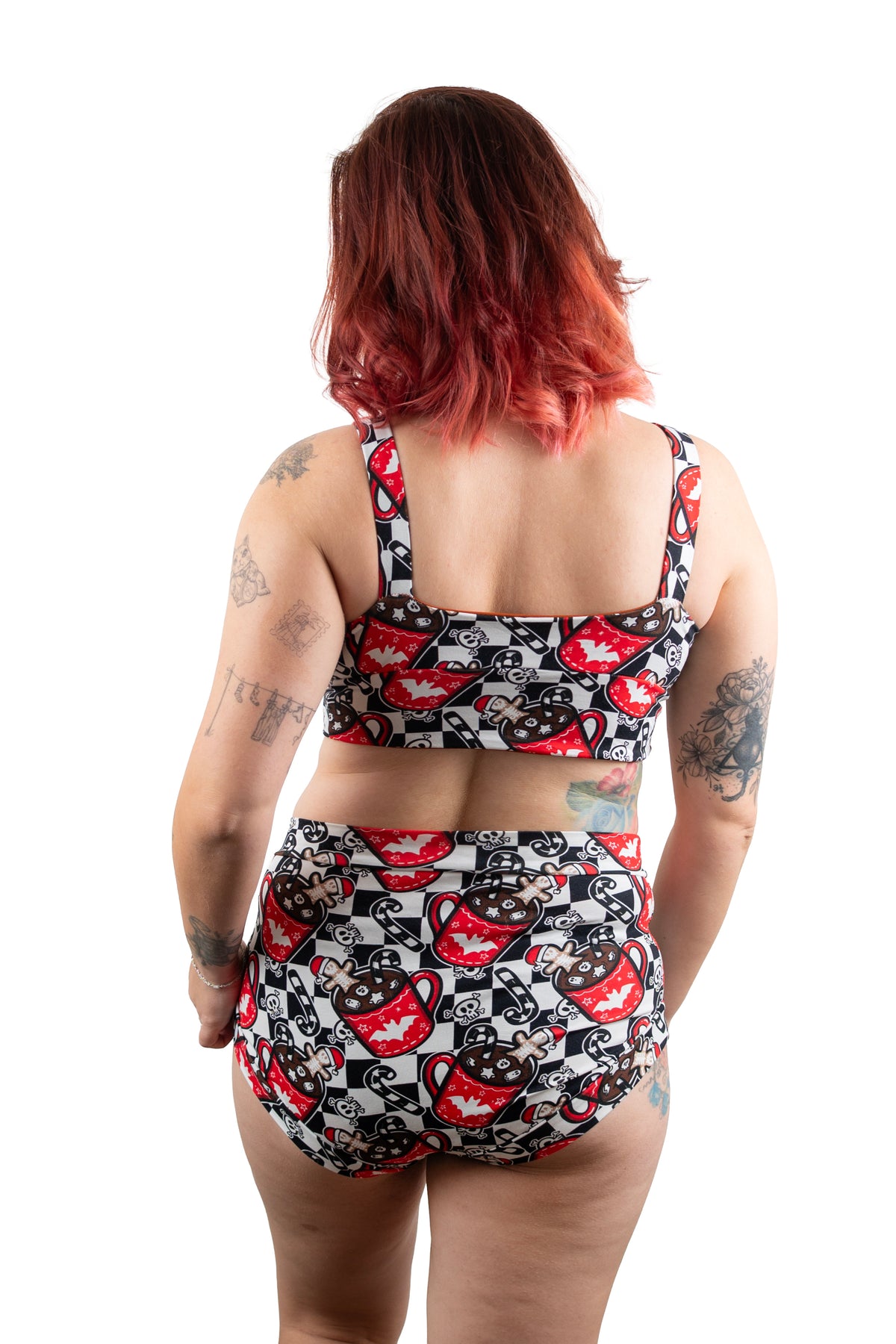 A woman viewed from behind wearing a two-piece bikini set with a black, white, and red graphic pattern. The pattern features cartoonish faces and abstract shapes.
