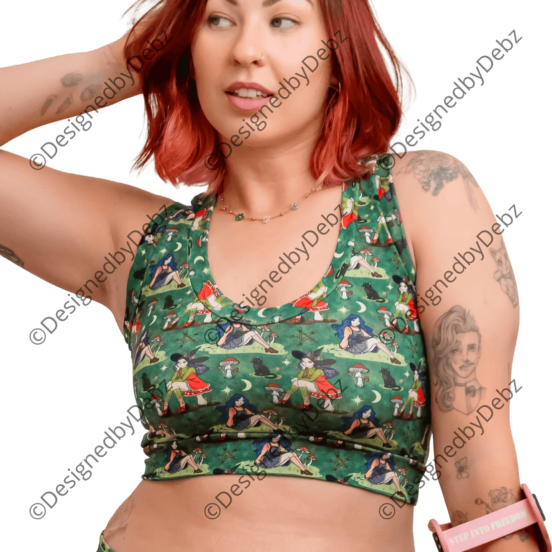 A woman with red hair models a matching green forest witch print activewear set consisting of a sports bra and shorts, holding a pink crutch against a solid white background.