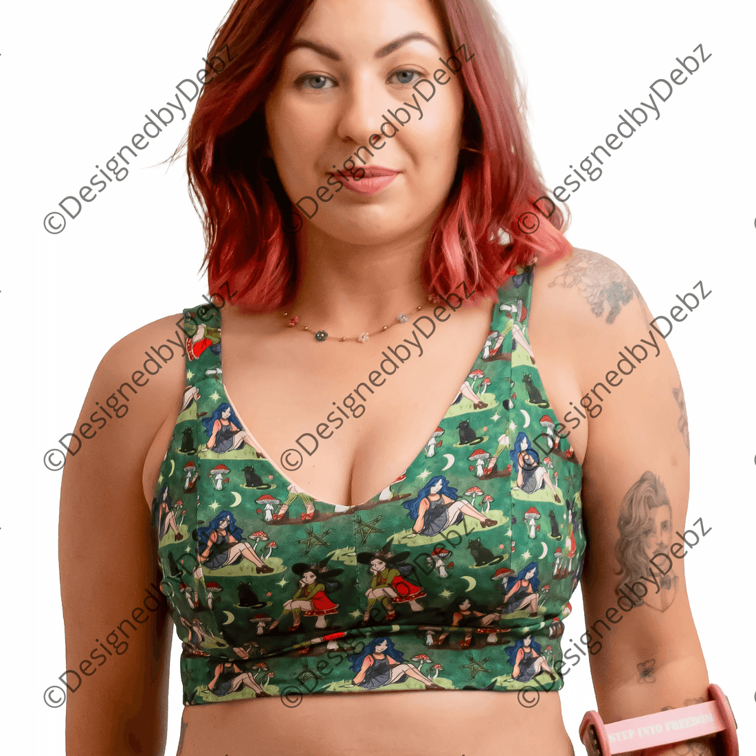 A woman with red hair wearing a green witch-print two-piece set consisting of a sports bra and high-waisted briefs, holding a pink crutch against a solid white background.
