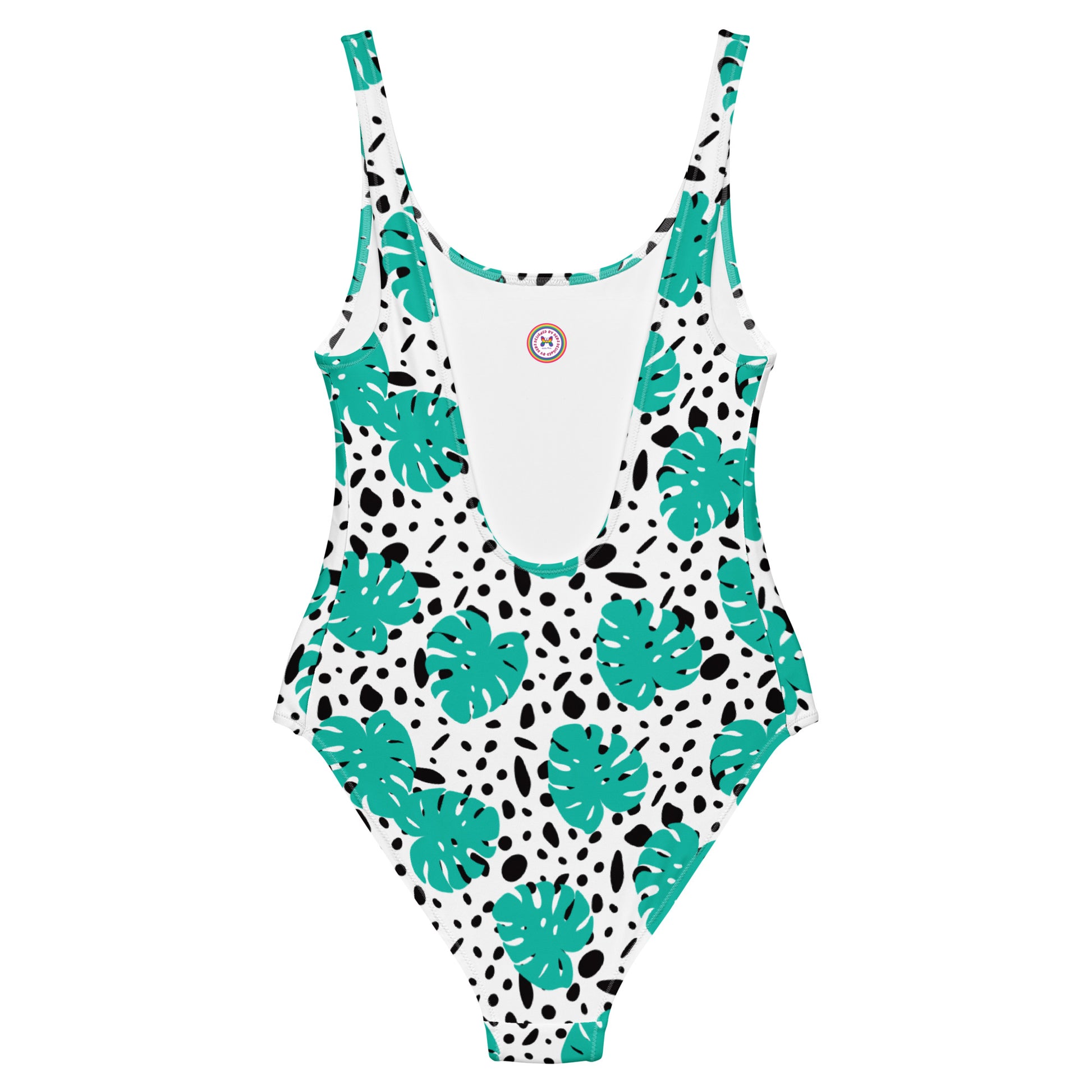 A one-piece swimsuit with a white base, featuring a pattern of teal monstera leaves and black irregular spots, shown flat against a white background.