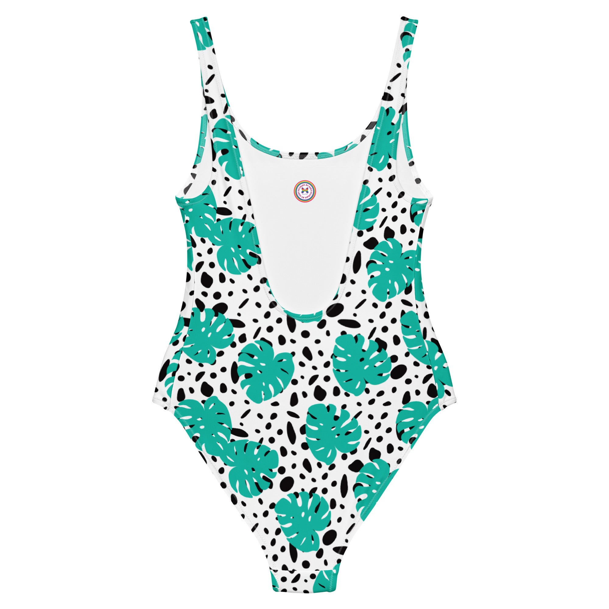 A one-piece swimsuit with a white base, featuring a pattern of teal monstera leaves and black irregular spots, shown flat against a white background.