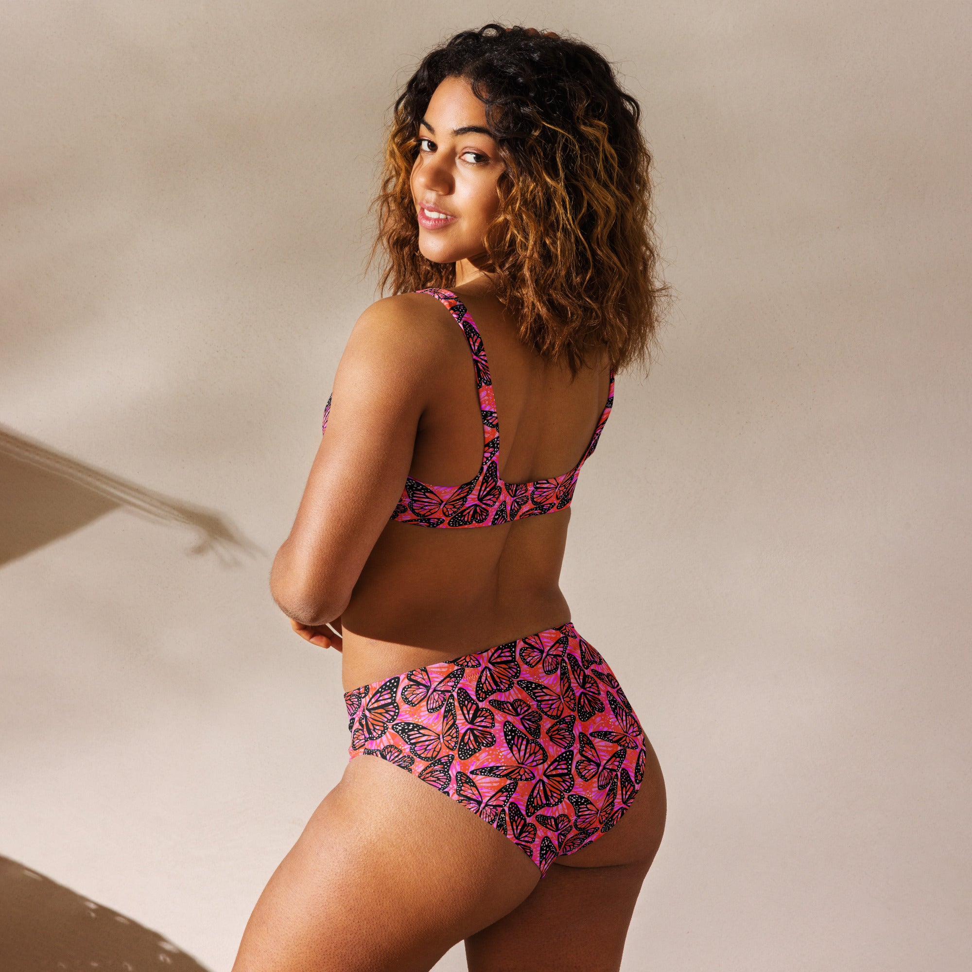 Recycled high-waisted bikini with butterfly print in pink and orange, featuring a white back, from Printful.