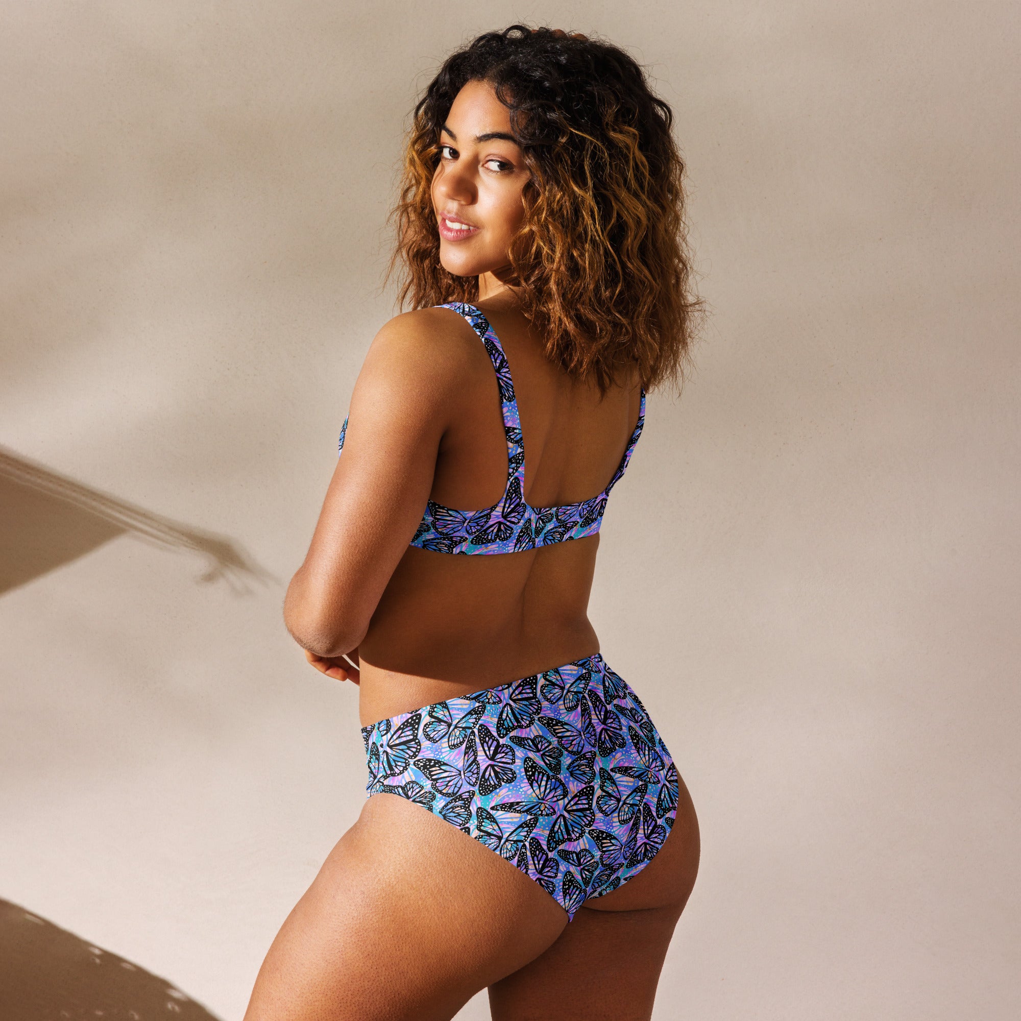 Recycled high-waisted bikini with butterfly print in pink and purple, shown from the back in a white background.