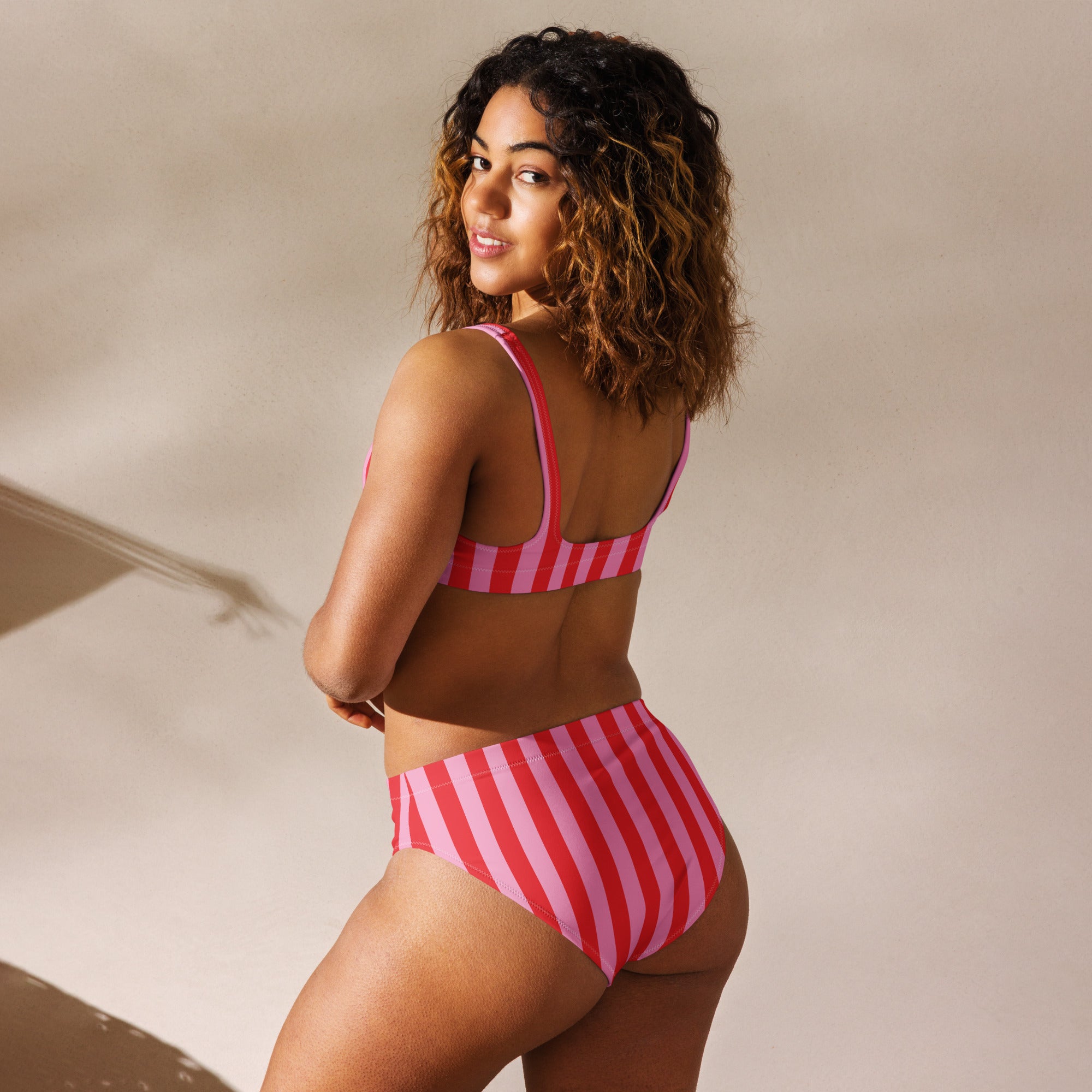 Recycled high-waisted bikini by Printful with pink and red stripe print, shown from the back in white.