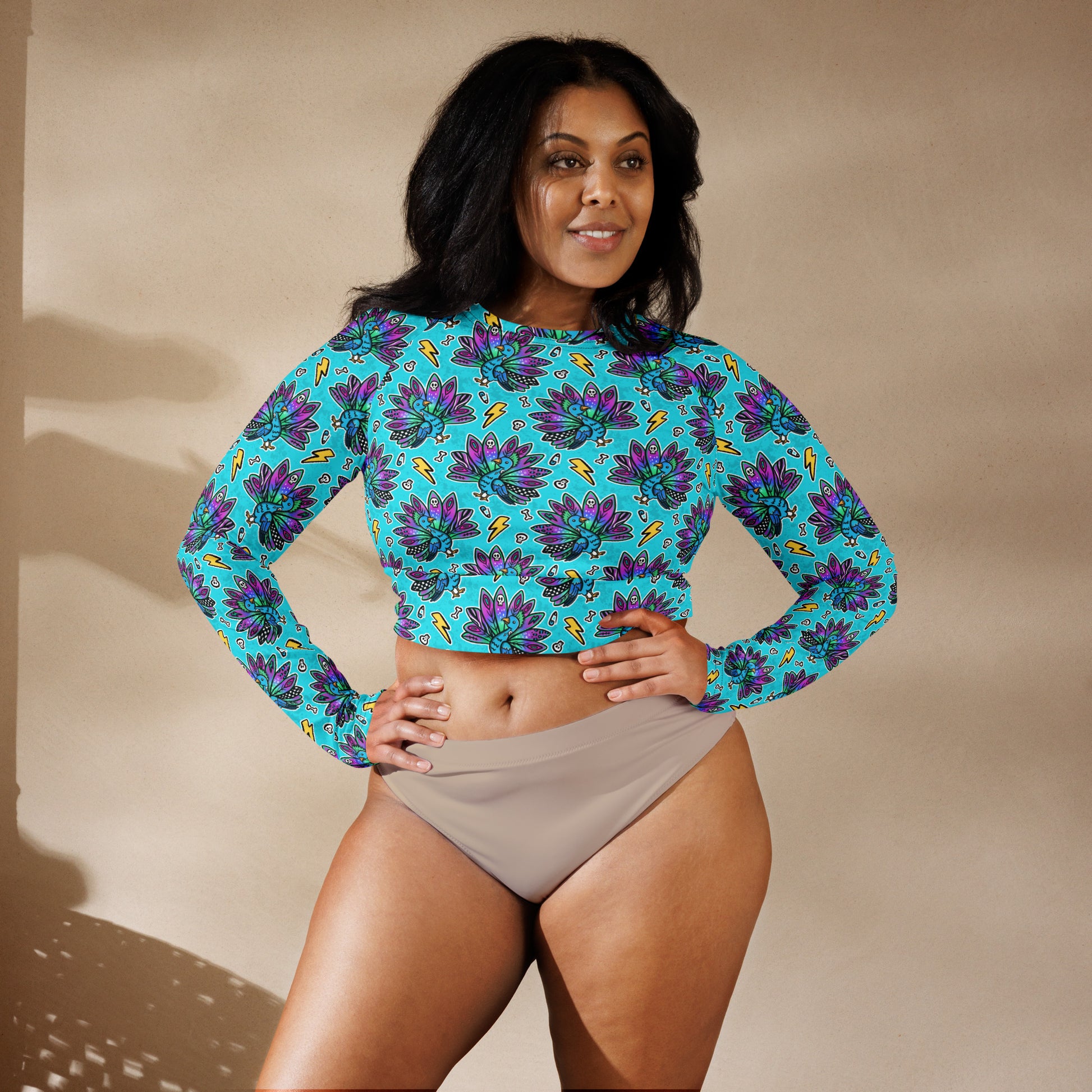 Electric peacock print rash guard crop top by Printful, long sleeve swimwear with UPF 50+ protection, made from recycled materials.