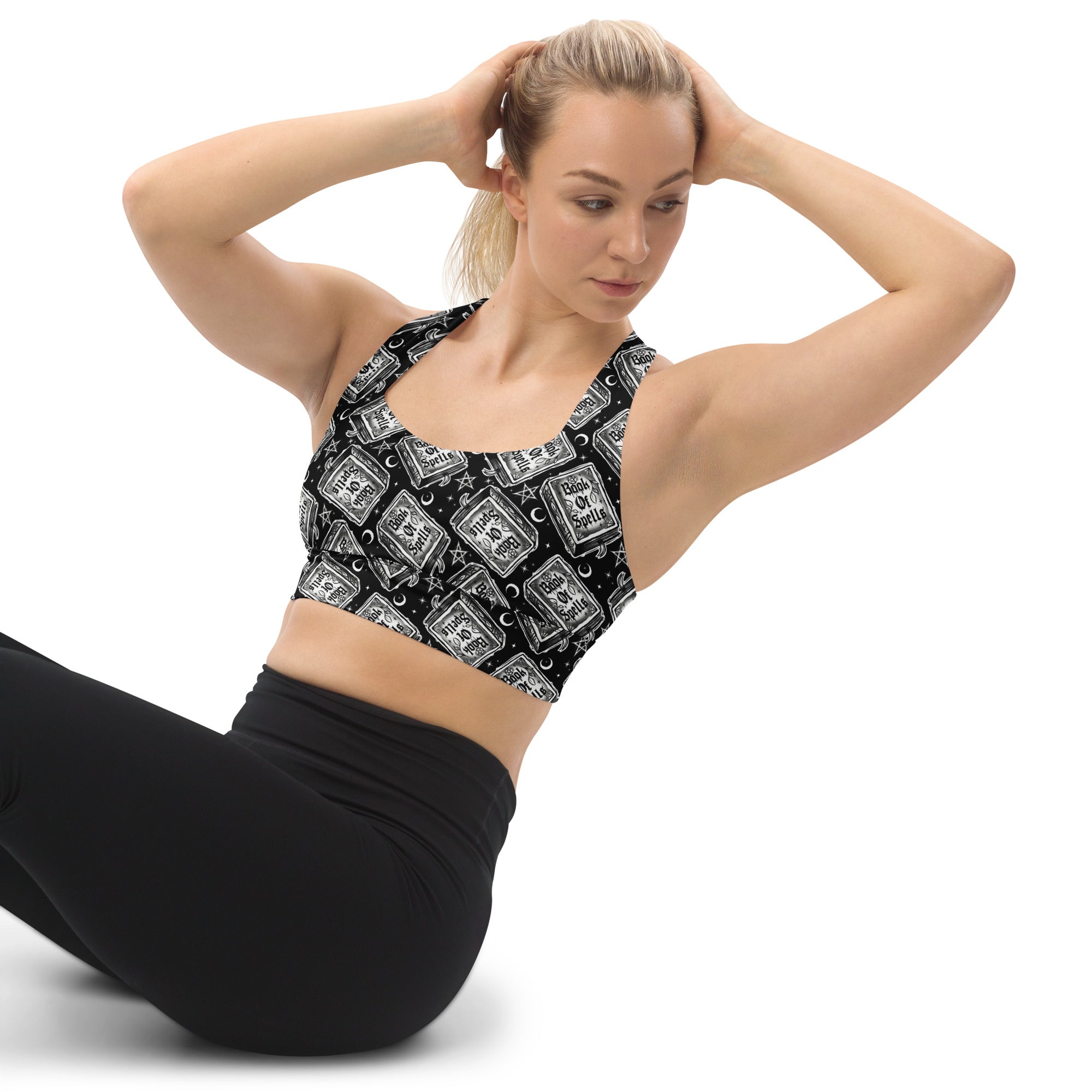 Printful Book of Spells recycled longline sports bra featuring all-over spell book print on white fabric, front view.