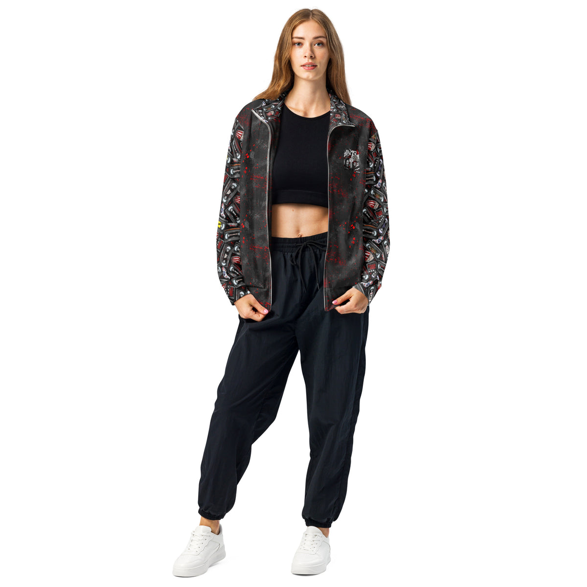 A woman modeling a black zip-up jacket with a red and white graffiti-style graphic print, paired with black jogger pants and white sneakers, against a solid white background.