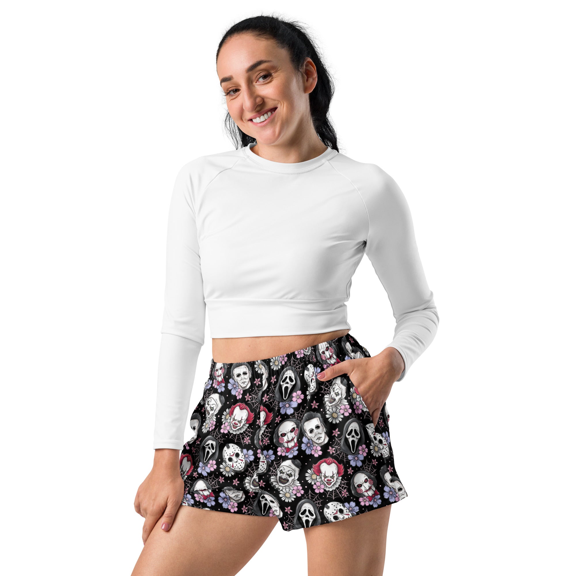 A woman modeling a white long-sleeve crop top and black shorts with a colourful Halloween character and floral pattern, set against a plain white background. Fetauring art the clown, it the clown and other horror villans!