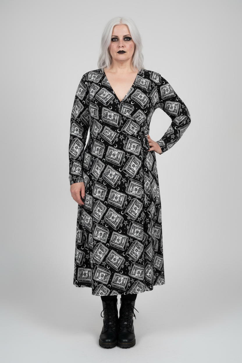 A model with silver hair and black makeup wearing a long-sleeved black midi dress with a white gothic-style graphic pattern, paired with black combat boots, against a light gray studio background.