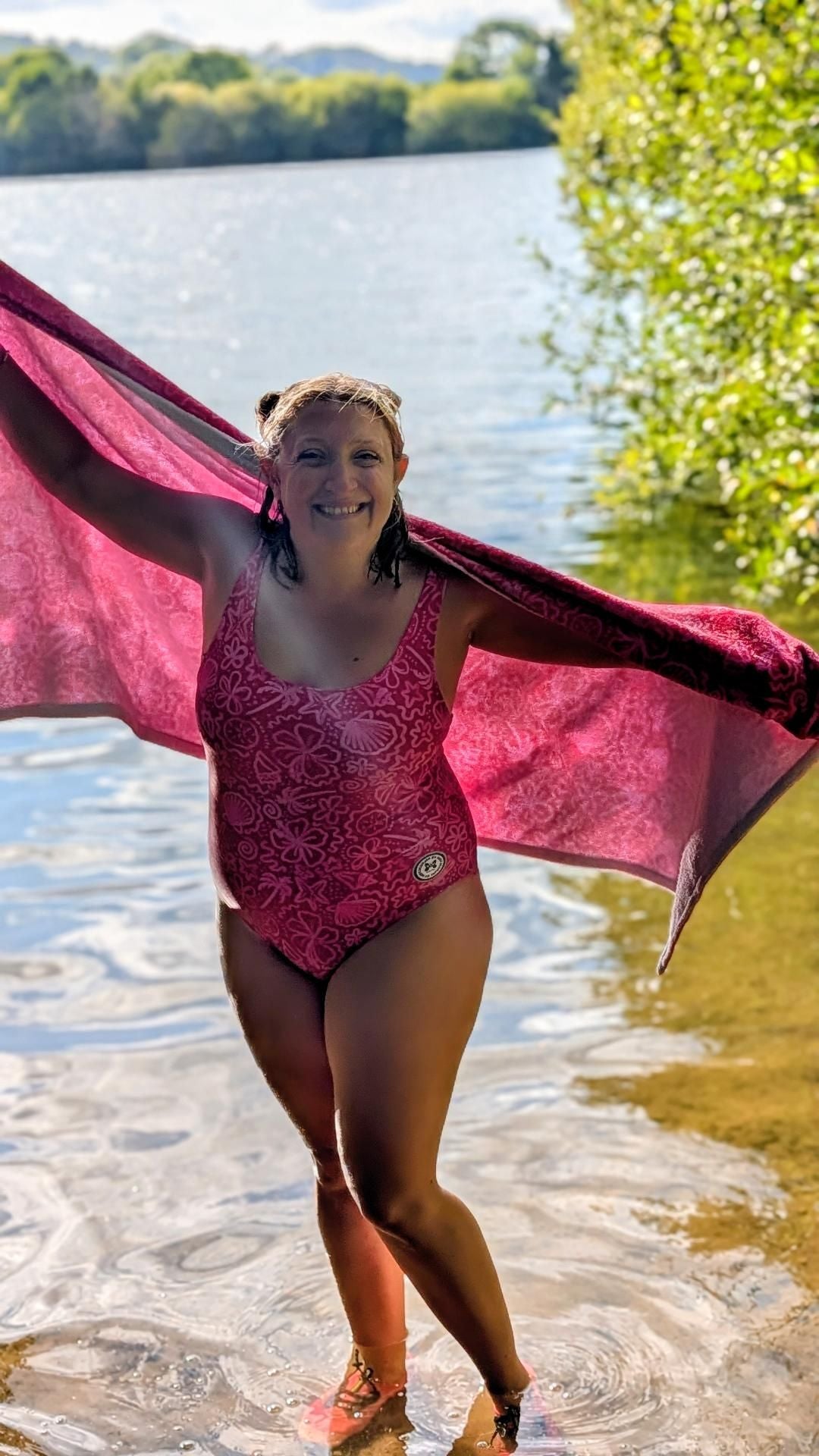 Bright pink one-piece swimsuit with palm tree and floral print, featuring sparkly sea shells design by Printful.