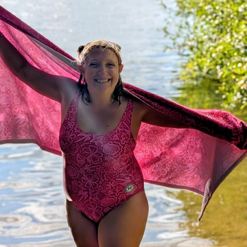 Bright pink one-piece swimsuit by Printful featuring palm trees, floral patterns, and sparkly seashell designs.