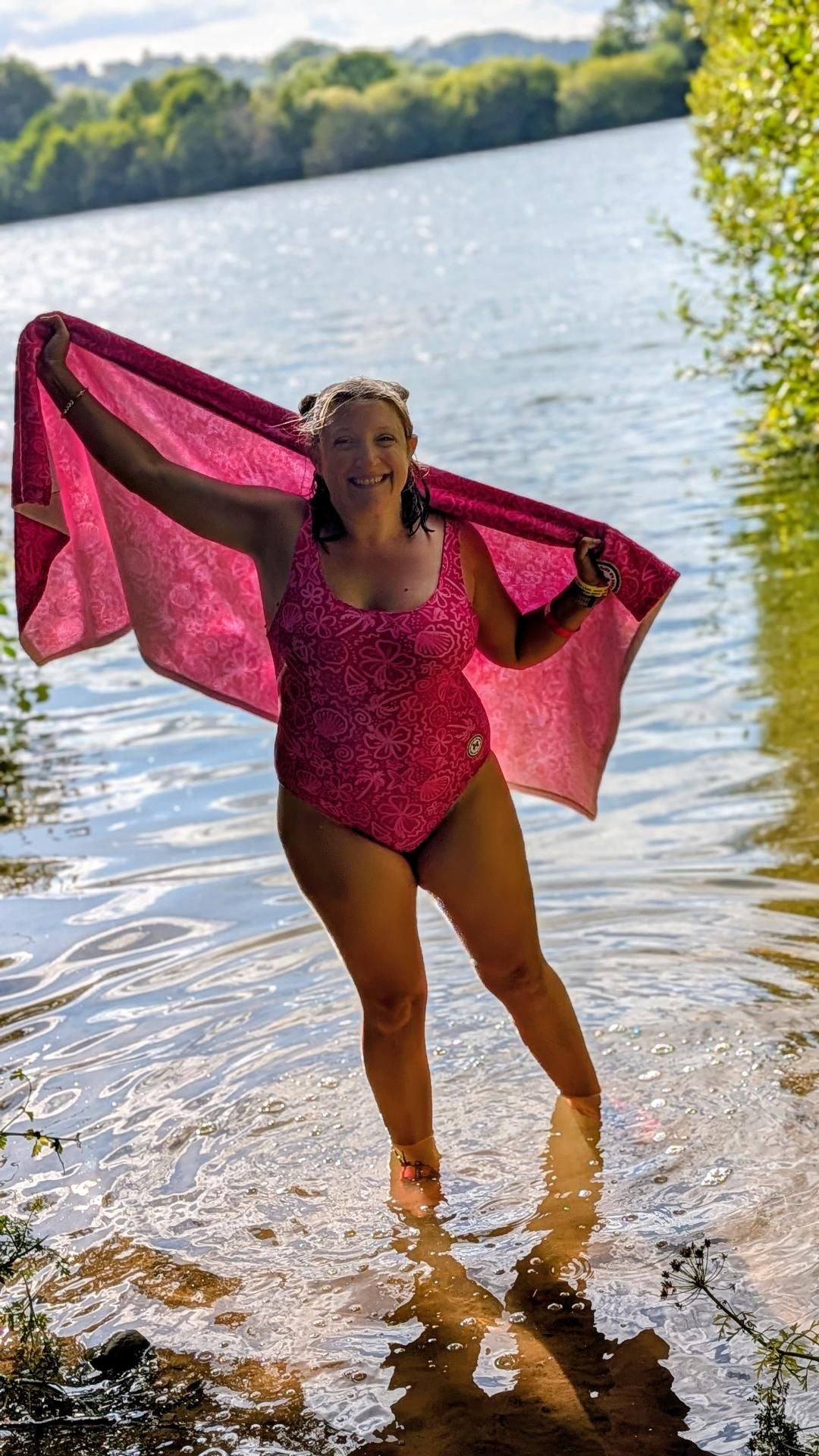 Bright pink one-piece swimsuit by Printful featuring palm trees, floral patterns, and sparkly seashell designs.