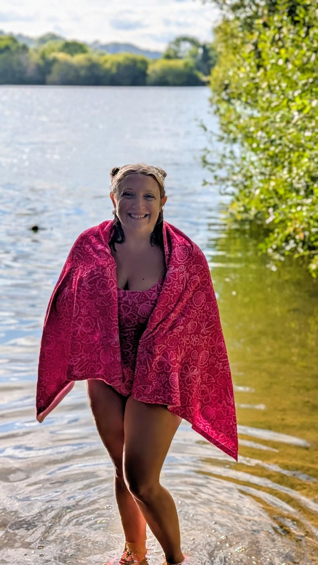 Bright pink one-piece swimsuit with palm tree and floral print, featuring seashell and sparkly swim design by Printful.