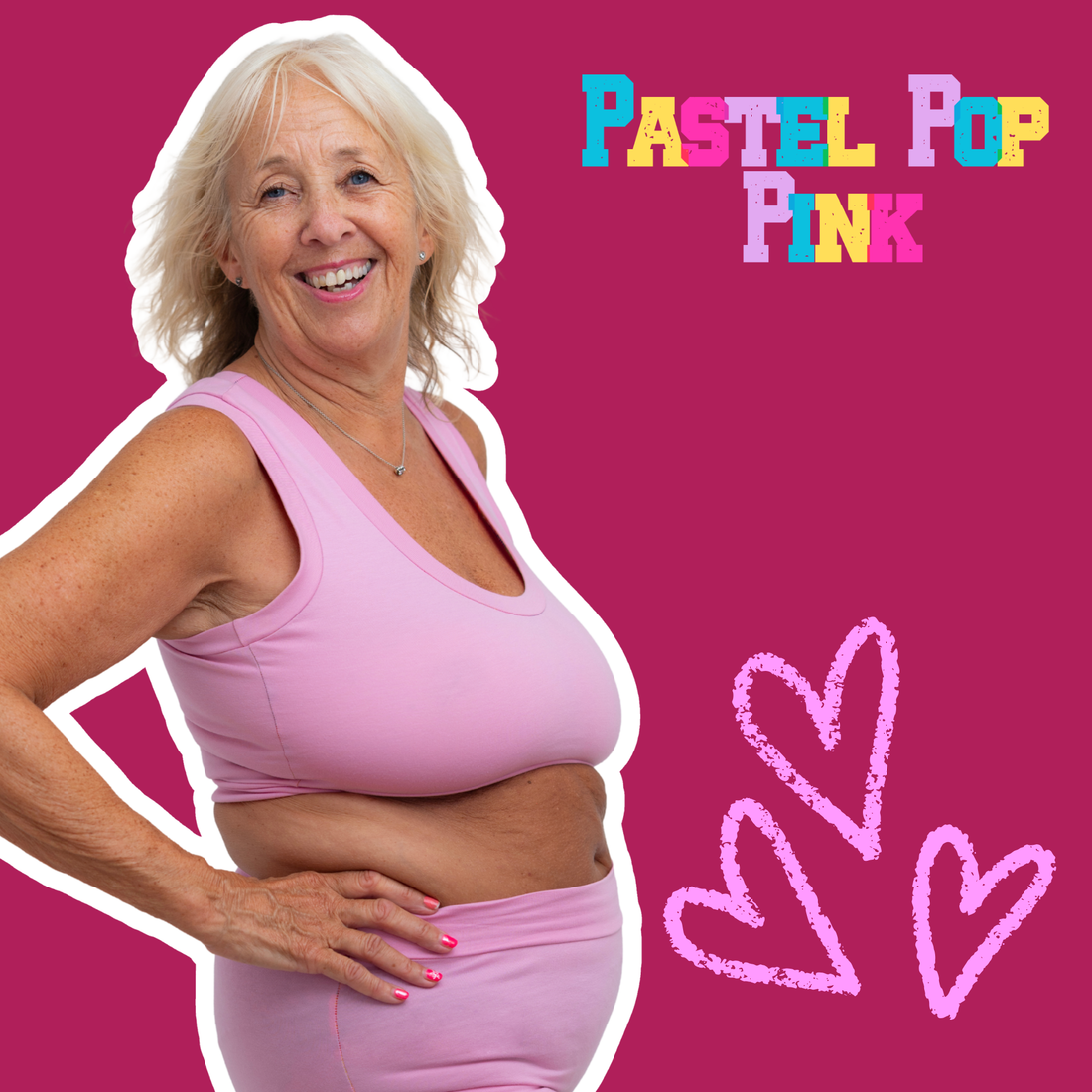 A smiling older woman with white hair wears a light pink sports bra and matching pink bottoms against a bright pink background, with the text 'PASTEL POP PINK' and pink heart doodles in the upper right.
