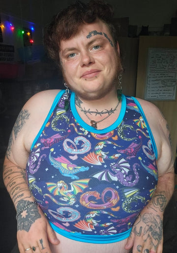 A person wearing a sleeveless binder alternative with a colourful psychedelic print featuring dragons, snakes, and hearts on a dark blue background with bright blue trim, photographed indoors.